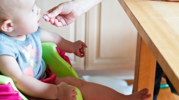 a baby being fed by hand in his high chair