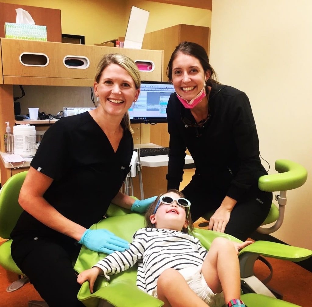 Child Laying in Dentist Chair Next to Dr. Dana Fox & Dental Assistant.