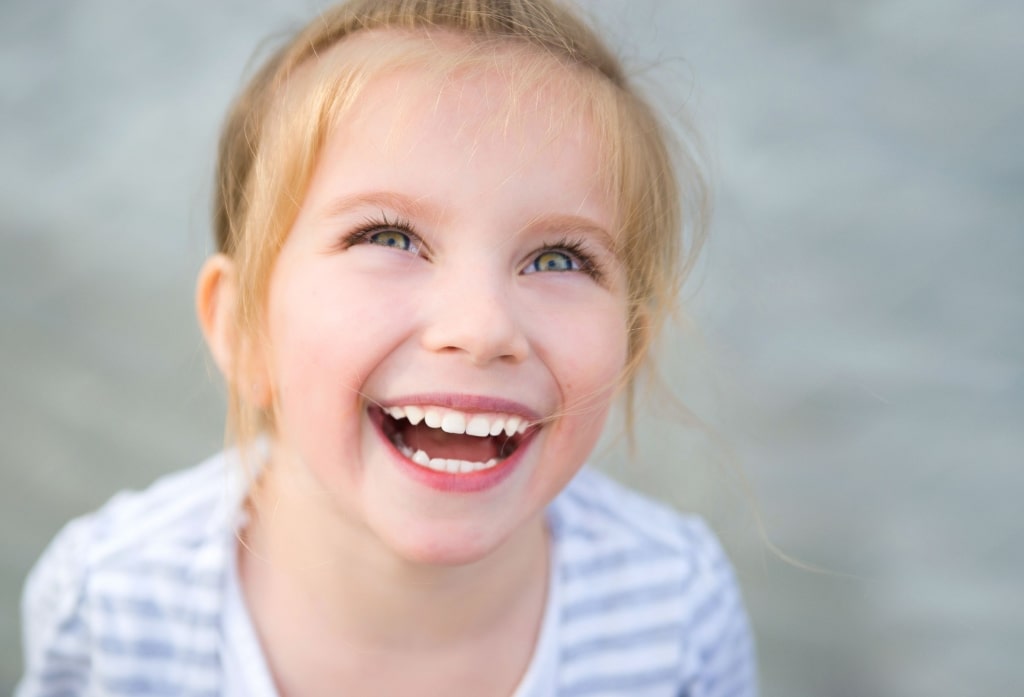 girl with blue eyes looking up and smiling showing her white teeth