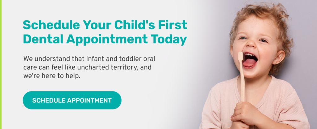 Toddler holding a wooden toothbrush to their mouth and smiling.